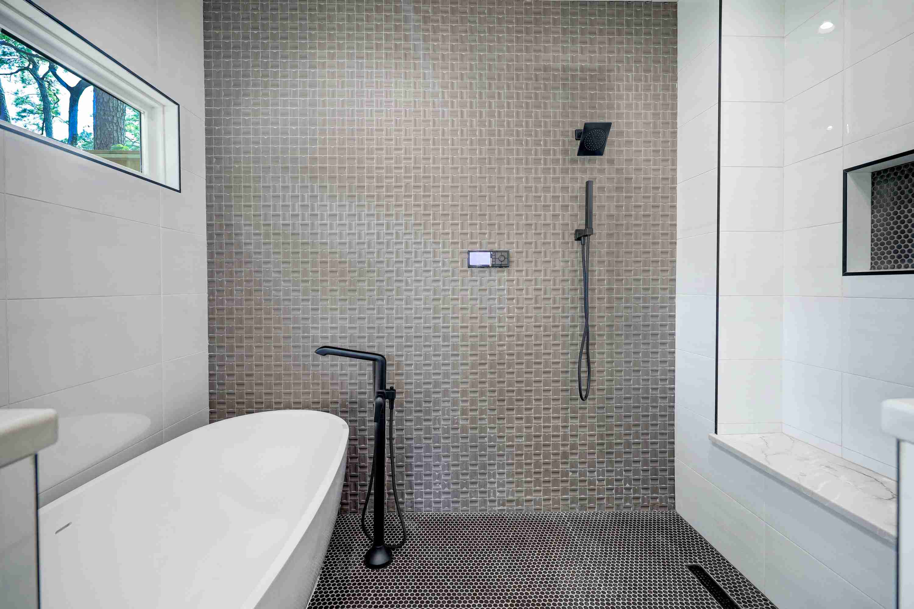 A modern bathroom with a glass-enclosed shower area featuring small gray tiles, and a freestanding white bathtub.
