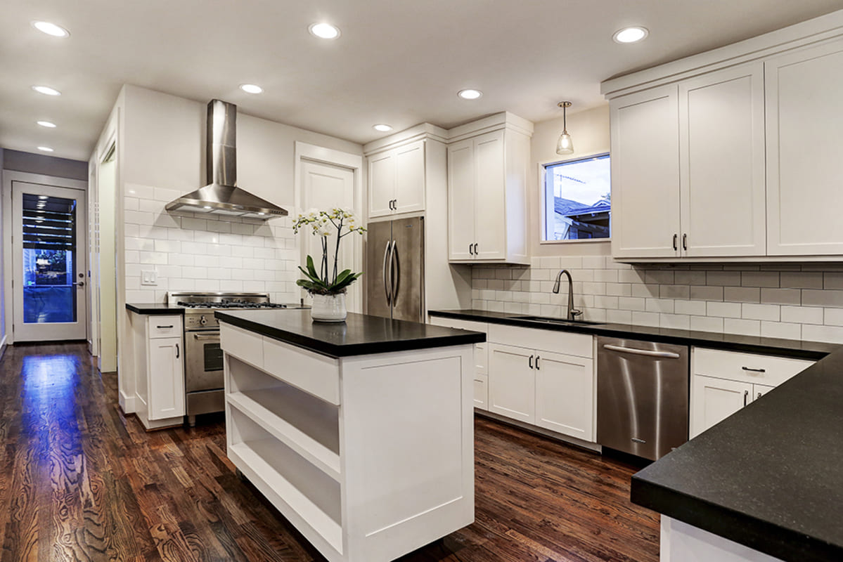 A Modern Farmhouse Kitchen With Black Countertops, White Cabinets, And A Custom Kitchen Island